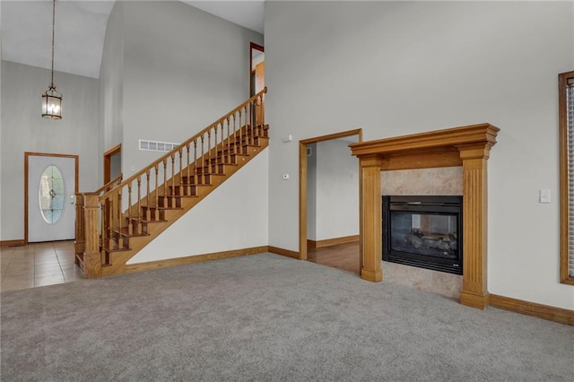 unfurnished living room featuring a high ceiling, a chandelier, light colored carpet, and a high end fireplace