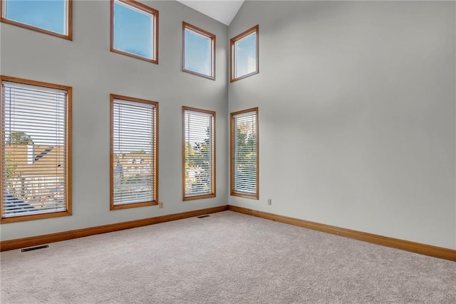 carpeted spare room with high vaulted ceiling