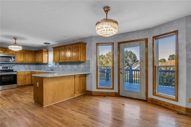 kitchen with appliances with stainless steel finishes, an inviting chandelier, hanging light fixtures, kitchen peninsula, and light wood-type flooring