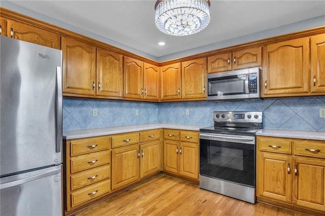 kitchen featuring an inviting chandelier, appliances with stainless steel finishes, light hardwood / wood-style floors, and decorative backsplash