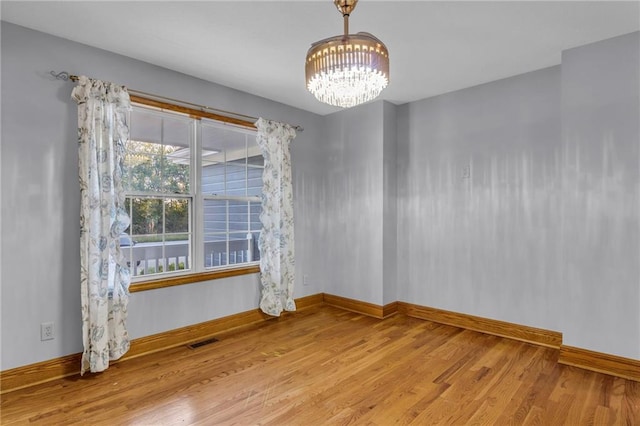 spare room featuring light wood-type flooring and an inviting chandelier