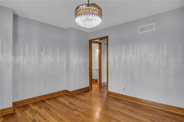 empty room with light hardwood / wood-style floors and a chandelier