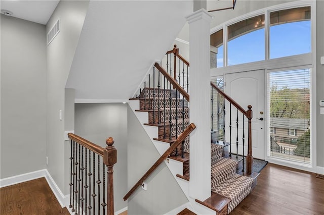 stairs with hardwood / wood-style flooring, ornate columns, and a towering ceiling