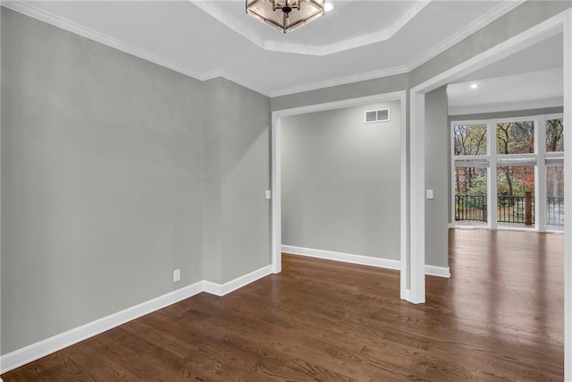 unfurnished room featuring a tray ceiling, an inviting chandelier, dark wood-type flooring, and ornamental molding