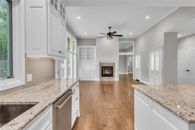 kitchen featuring white cabinets, stainless steel dishwasher, light stone countertops, tasteful backsplash, and light hardwood / wood-style floors