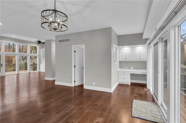 unfurnished living room featuring a wealth of natural light, dark hardwood / wood-style flooring, built in desk, and ceiling fan with notable chandelier