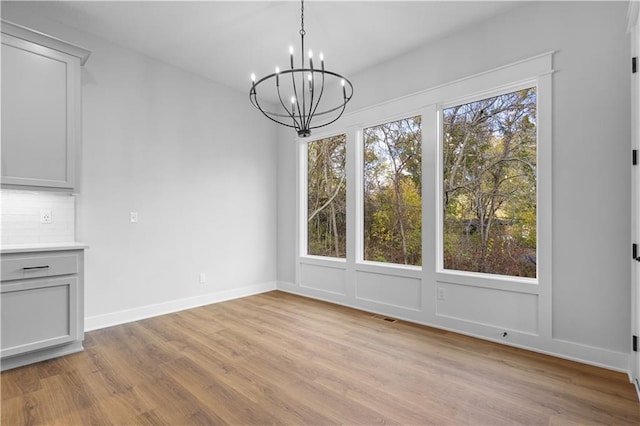 unfurnished dining area featuring an inviting chandelier and light hardwood / wood-style floors