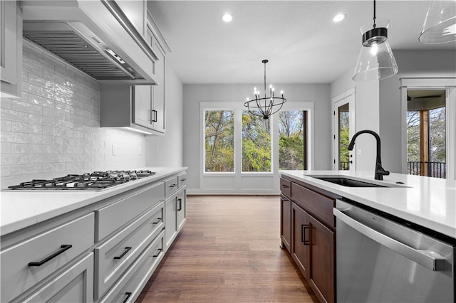 kitchen featuring white cabinetry, appliances with stainless steel finishes, wood-type flooring, a notable chandelier, and wall chimney range hood