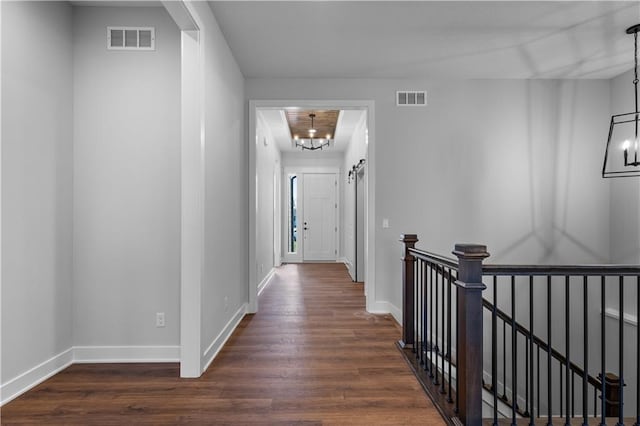 hallway with an inviting chandelier, a barn door, and dark hardwood / wood-style floors