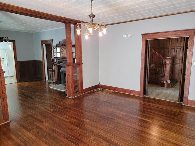 unfurnished dining area featuring an inviting chandelier, dark hardwood / wood-style flooring, decorative columns, and crown molding