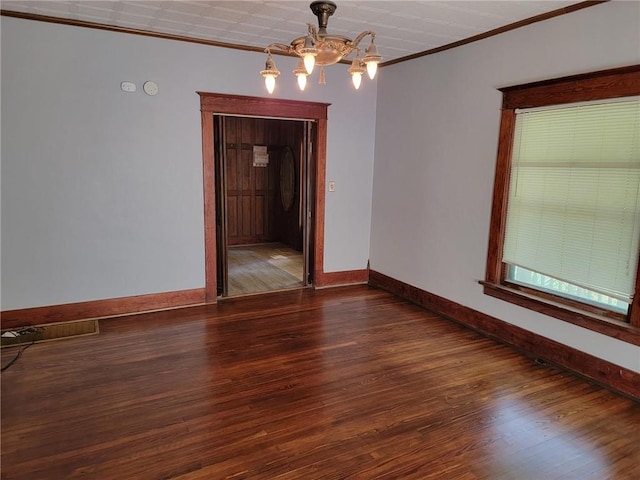 spare room with dark wood-type flooring, ornamental molding, and an inviting chandelier