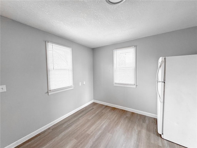 empty room featuring a textured ceiling, baseboards, and wood finished floors