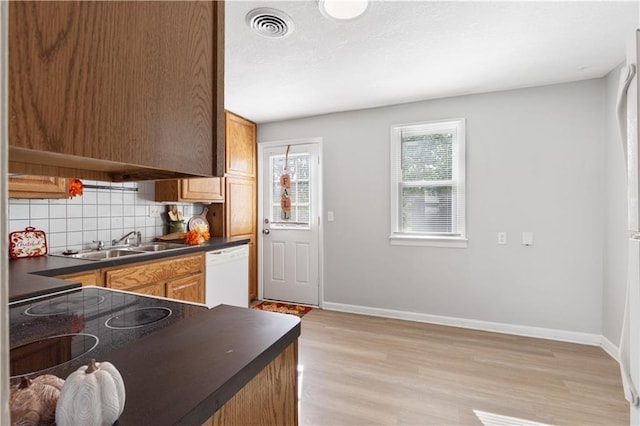 kitchen with a sink, light wood-style floors, decorative backsplash, dishwasher, and dark countertops