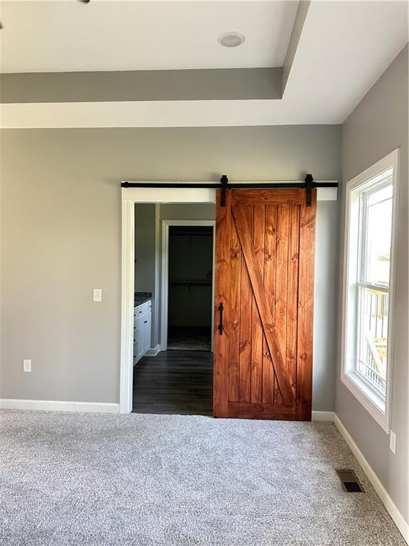 unfurnished bedroom with ensuite bathroom, a barn door, dark carpet, and multiple windows