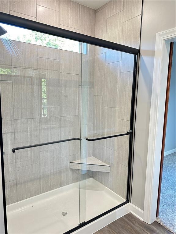 full bath with a stall shower, baseboards, and wood finished floors