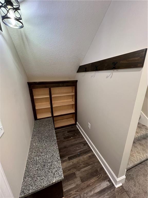 hallway with dark wood finished floors, vaulted ceiling, a textured ceiling, and baseboards