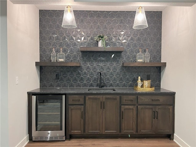 bar featuring wine cooler, sink, decorative backsplash, and dark stone countertops