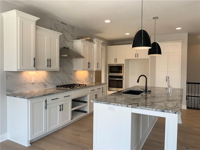 kitchen featuring appliances with stainless steel finishes, decorative light fixtures, sink, white cabinets, and a center island with sink