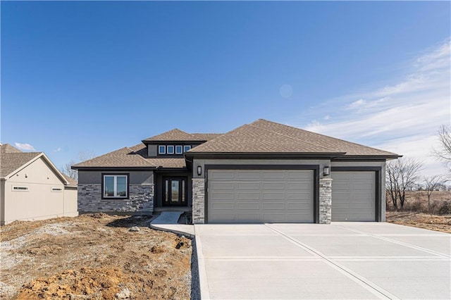 prairie-style home featuring an attached garage, a shingled roof, driveway, stone siding, and stucco siding