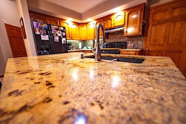 kitchen with backsplash, black refrigerator with ice dispenser, and sink