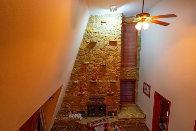 living room with ceiling fan, a stone fireplace, and vaulted ceiling