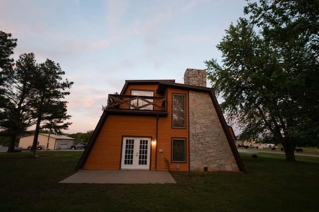 back house at dusk featuring french doors, a yard, a balcony, and a patio