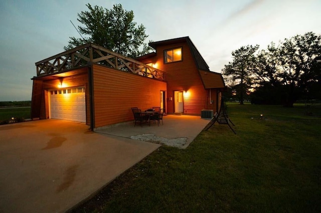 back house at dusk featuring a lawn and a patio area