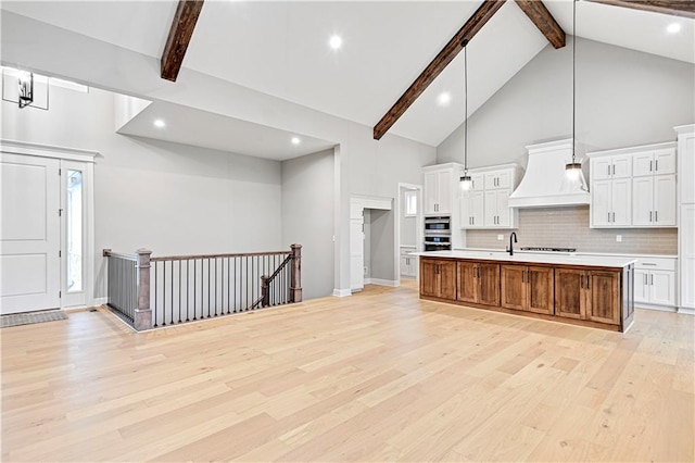 kitchen featuring a large island with sink, hanging light fixtures, light wood-type flooring, beamed ceiling, and white cabinetry