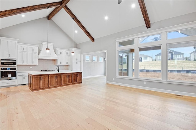 kitchen featuring white cabinetry, light hardwood / wood-style flooring, high vaulted ceiling, a spacious island, and custom exhaust hood