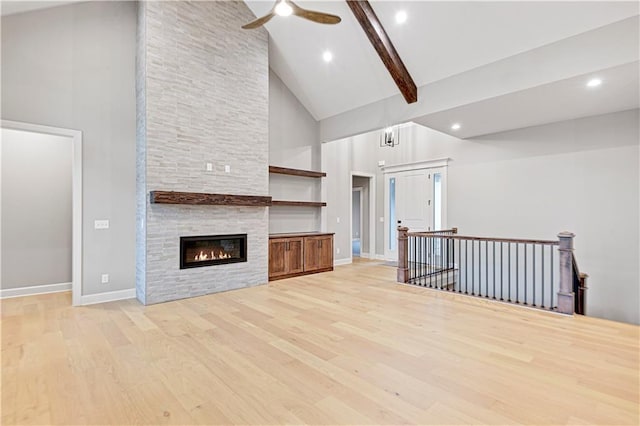 unfurnished living room featuring beam ceiling, light wood-type flooring, high vaulted ceiling, and a stone fireplace