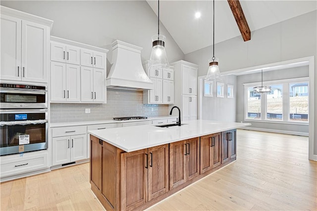 kitchen featuring sink, white cabinets, an island with sink, and custom range hood