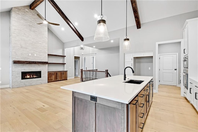 kitchen with a center island with sink, white cabinets, sink, and beamed ceiling