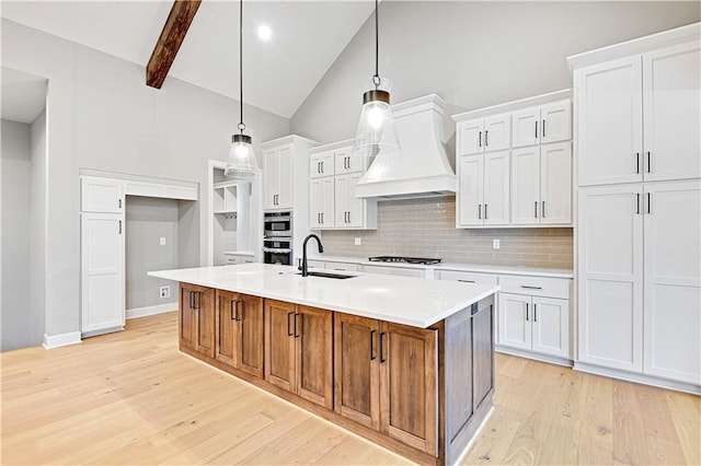 kitchen featuring white cabinetry, sink, high vaulted ceiling, an island with sink, and decorative light fixtures