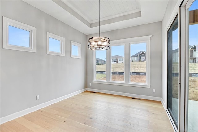 unfurnished dining area with a tray ceiling, crown molding, an inviting chandelier, and light wood-type flooring