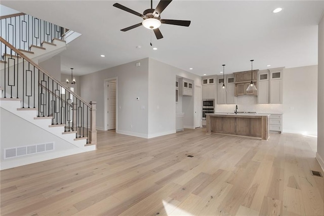 unfurnished living room with ceiling fan with notable chandelier, sink, and light wood-type flooring