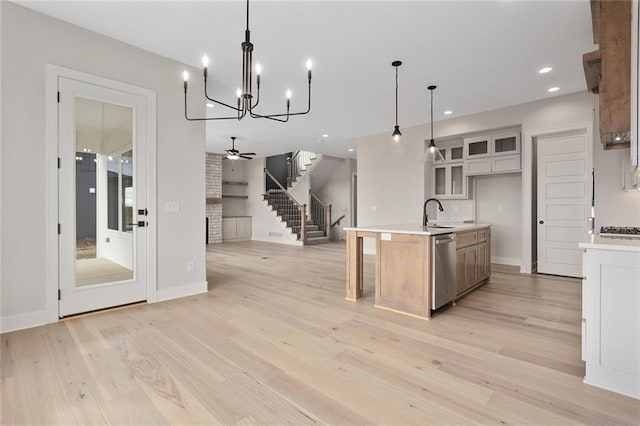 kitchen featuring a center island with sink, decorative light fixtures, light hardwood / wood-style flooring, stainless steel dishwasher, and ceiling fan with notable chandelier