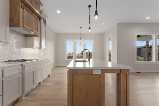 kitchen with white cabinets, stainless steel gas stovetop, a kitchen island with sink, and sink