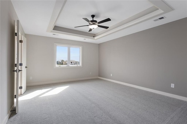 spare room featuring light colored carpet, ceiling fan, and a tray ceiling