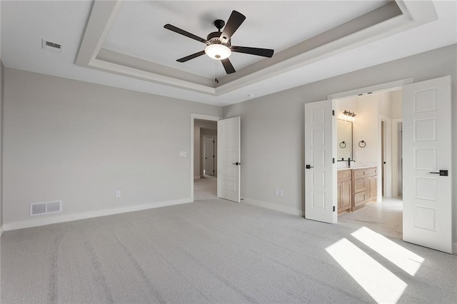 unfurnished bedroom with connected bathroom, light carpet, ceiling fan, and a raised ceiling