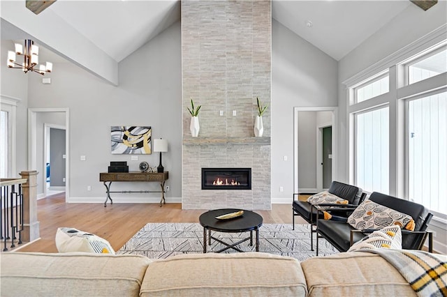 living room featuring wood-type flooring, high vaulted ceiling, a notable chandelier, and a tiled fireplace