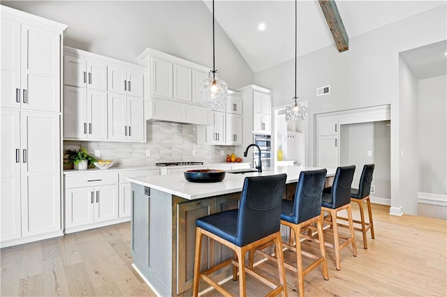 kitchen with a kitchen bar, tasteful backsplash, pendant lighting, a center island with sink, and white cabinetry