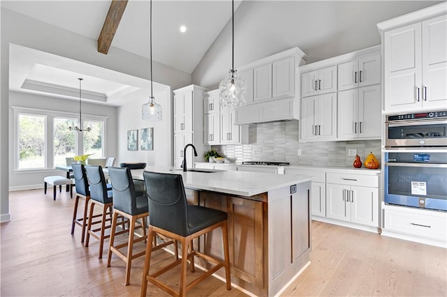 kitchen featuring tasteful backsplash, stainless steel double oven, a kitchen island with sink, sink, and white cabinetry