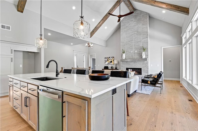 kitchen with light stone countertops, sink, hanging light fixtures, stainless steel dishwasher, and an island with sink