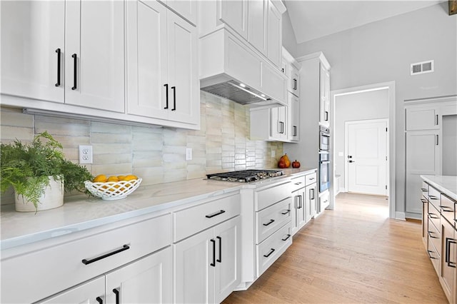 kitchen with light stone countertops, tasteful backsplash, stainless steel appliances, light hardwood / wood-style flooring, and white cabinetry