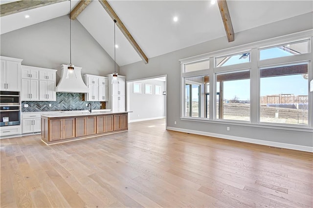 kitchen featuring light wood-style flooring, backsplash, open floor plan, double oven, and light countertops