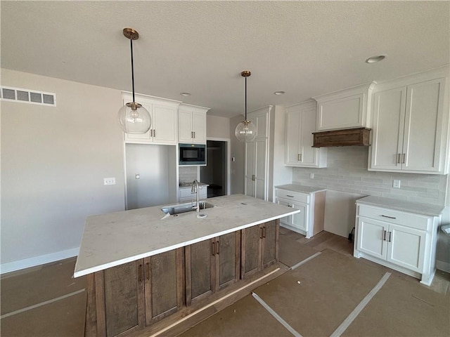 kitchen featuring built in microwave, white cabinetry, sink, pendant lighting, and a center island with sink