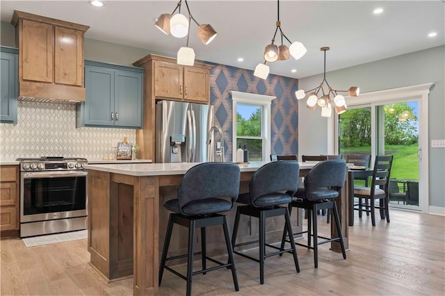 kitchen with a kitchen island with sink, hanging light fixtures, a notable chandelier, appliances with stainless steel finishes, and light hardwood / wood-style floors