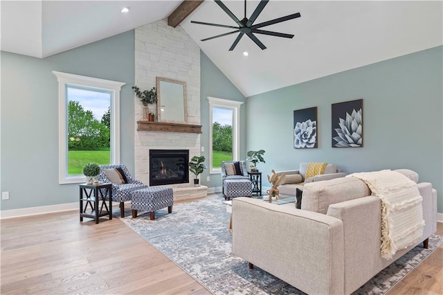 living room featuring high vaulted ceiling, light wood-type flooring, beamed ceiling, ceiling fan, and a fireplace