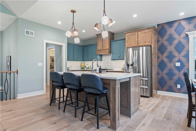 kitchen featuring sink, light wood-type flooring, hanging light fixtures, stainless steel fridge with ice dispenser, and a kitchen island with sink