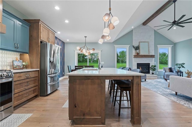 kitchen featuring appliances with stainless steel finishes, vaulted ceiling with beams, light wood-type flooring, pendant lighting, and a center island with sink